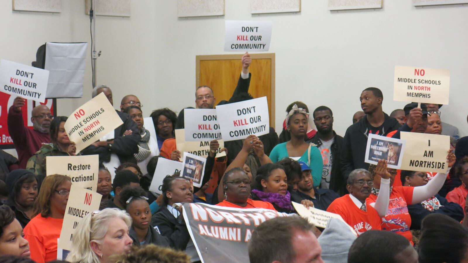 People hold aloft signs at school closings meeting.