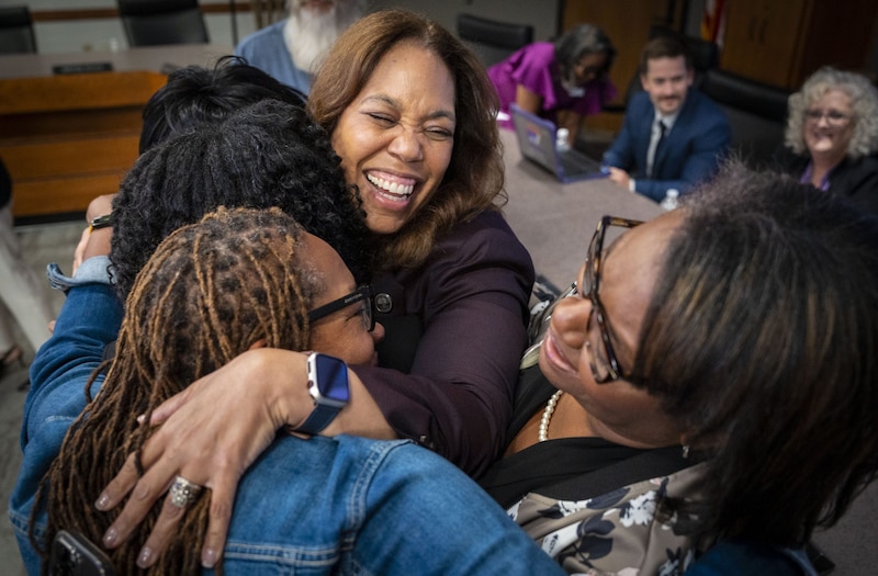 A photograph of four Black women hugging and celebrating inside of a conference room.