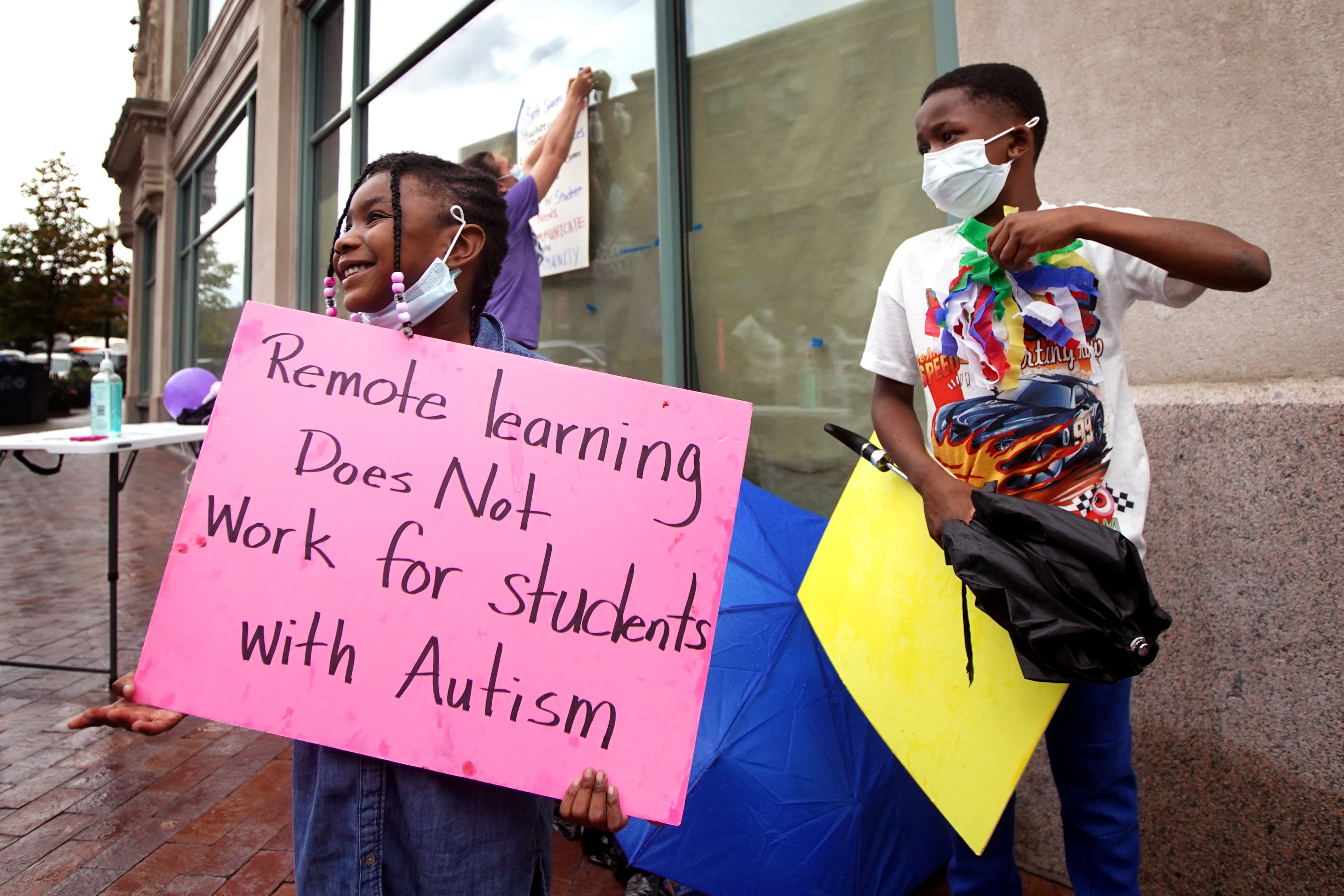A girl holds a sign at a protest that reads: Remote learning does not work for students with autism.
