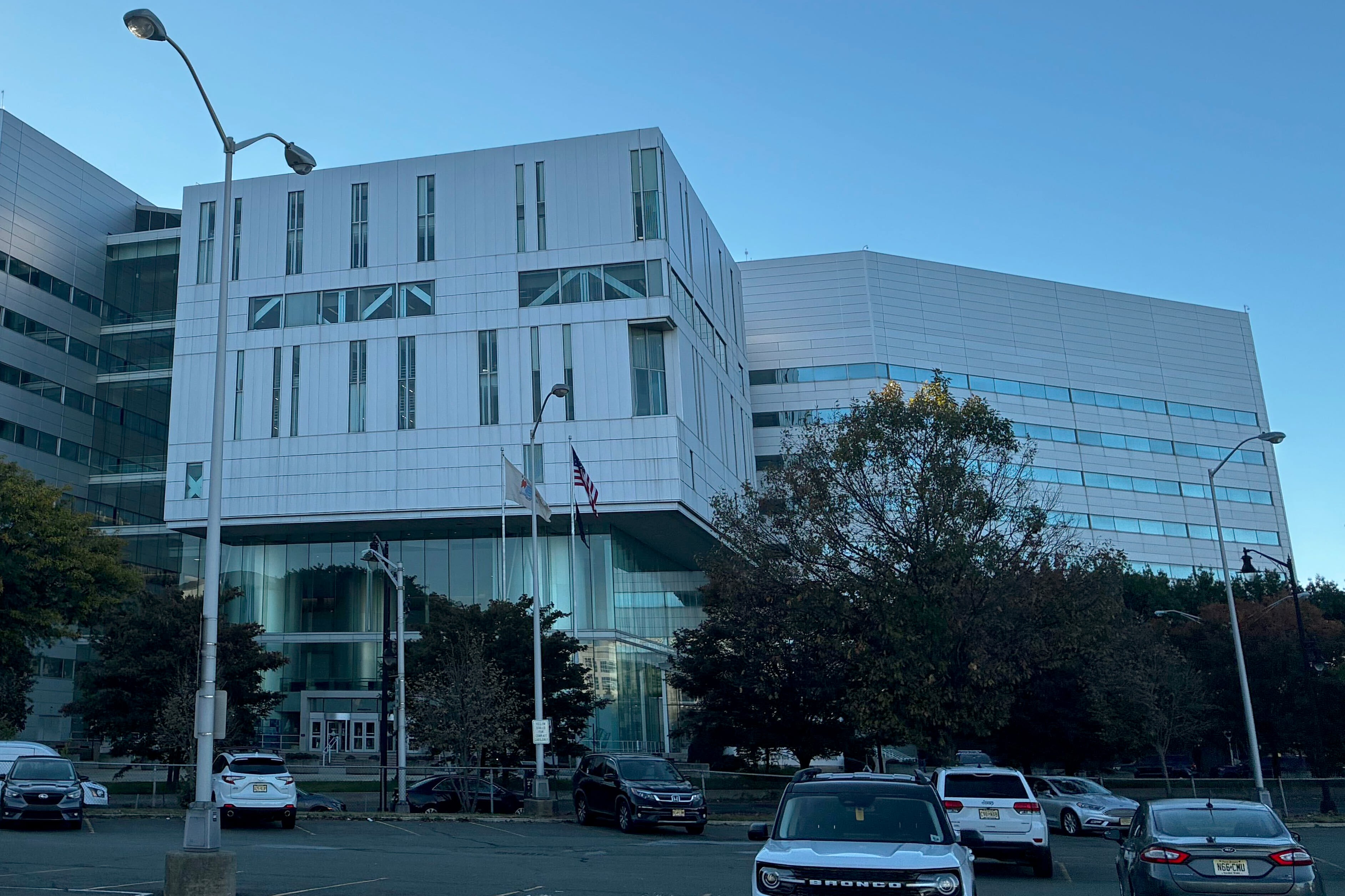 The outside of a large glass building with a parking lot in the foreground and all before the sun is fully up.
