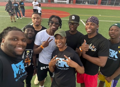 A group of students and a teacher pose for a photo on a football field.