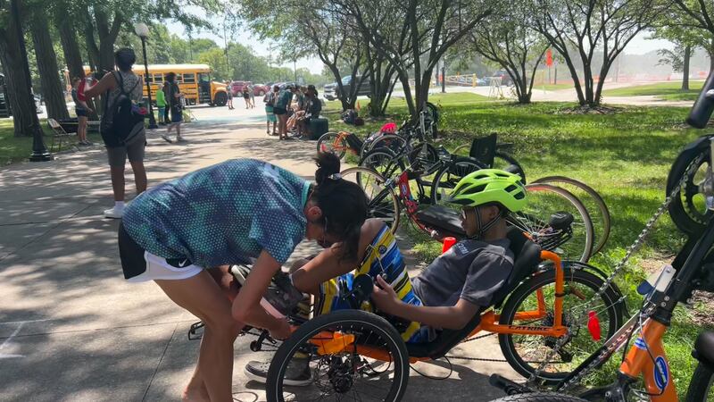 A woman is helping a boy wearing a helmet get situated on a bike adapted for children with disabilities.