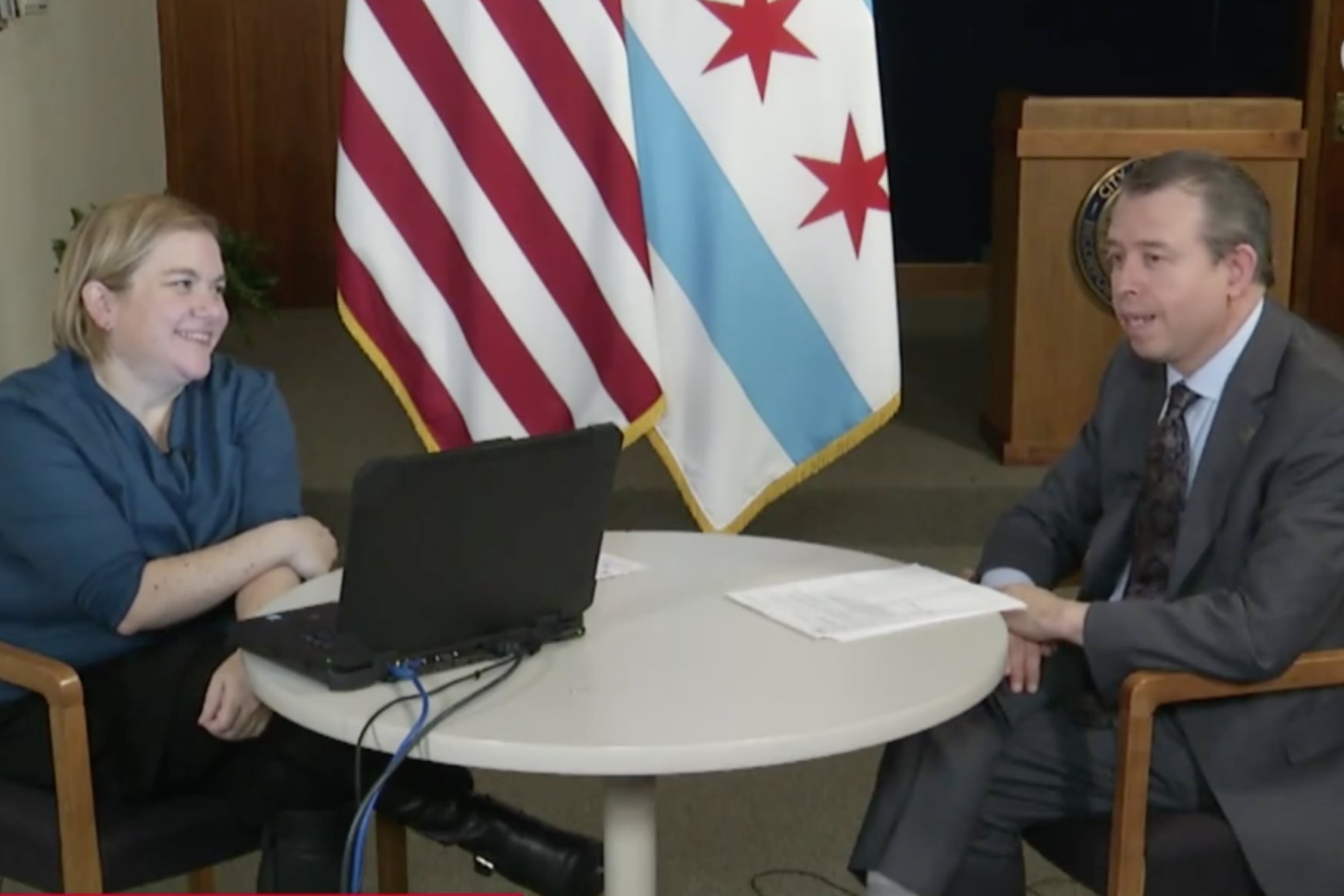 A woman and man sit at a table in front of the American and Chicago flags.