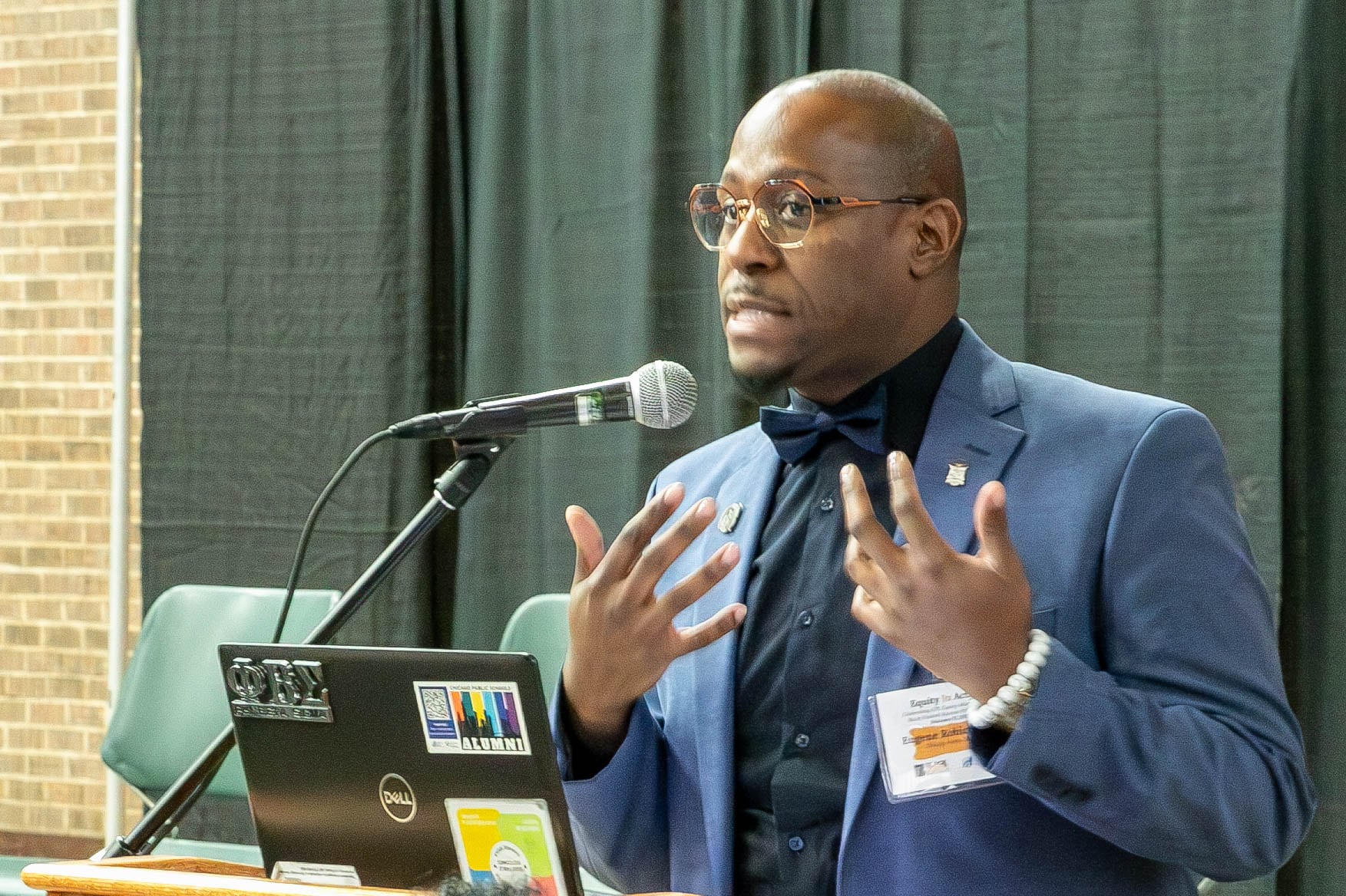 A man with a blue suit jacket, shirt and tie gestures while speaking.