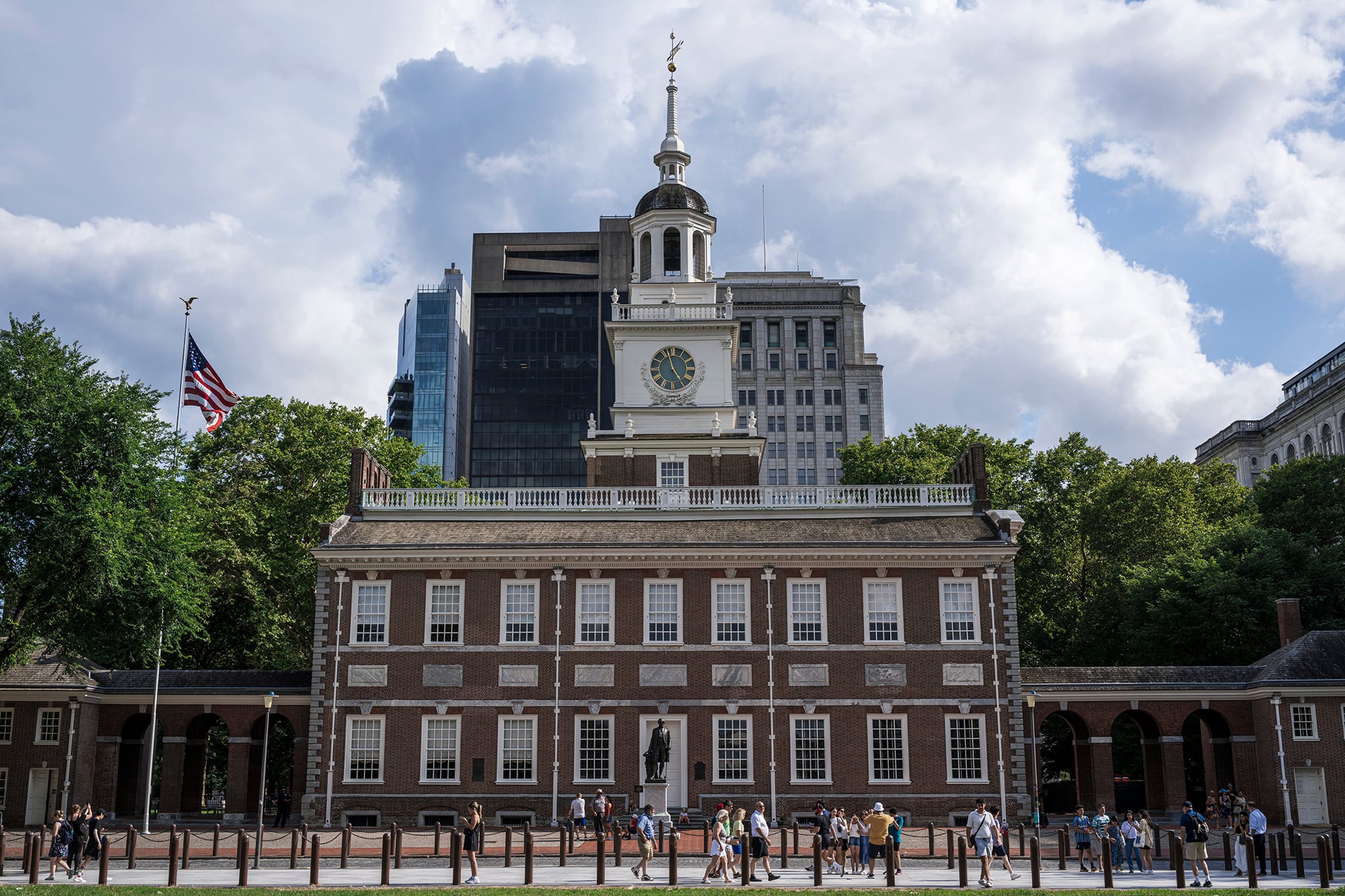 A photograph of the front entrance of the Independence Hall at Philadelphia on a cloudy, sunny day with a group of people outside on the sidewalk.