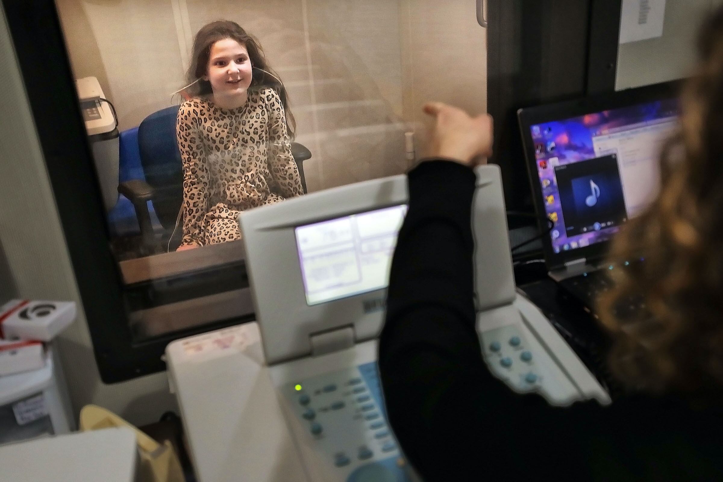 An 8-year-old girl takes a hearing test with the help of a woman audiologist.