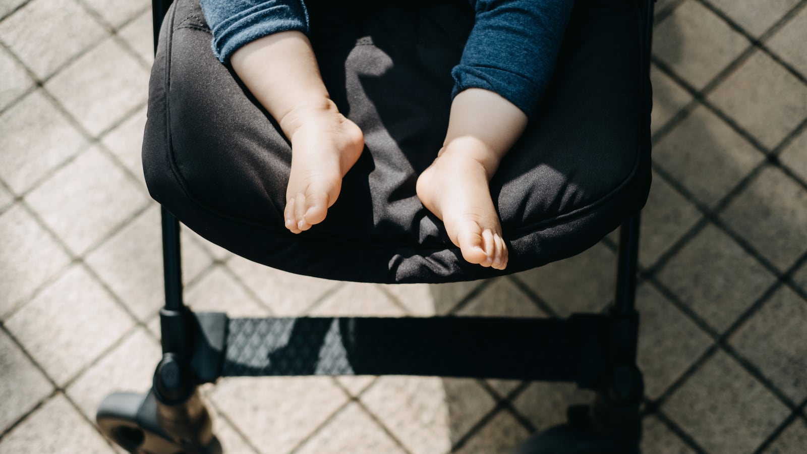 Low section of baby feet resting in baby stroller on street with warmth of sunlight