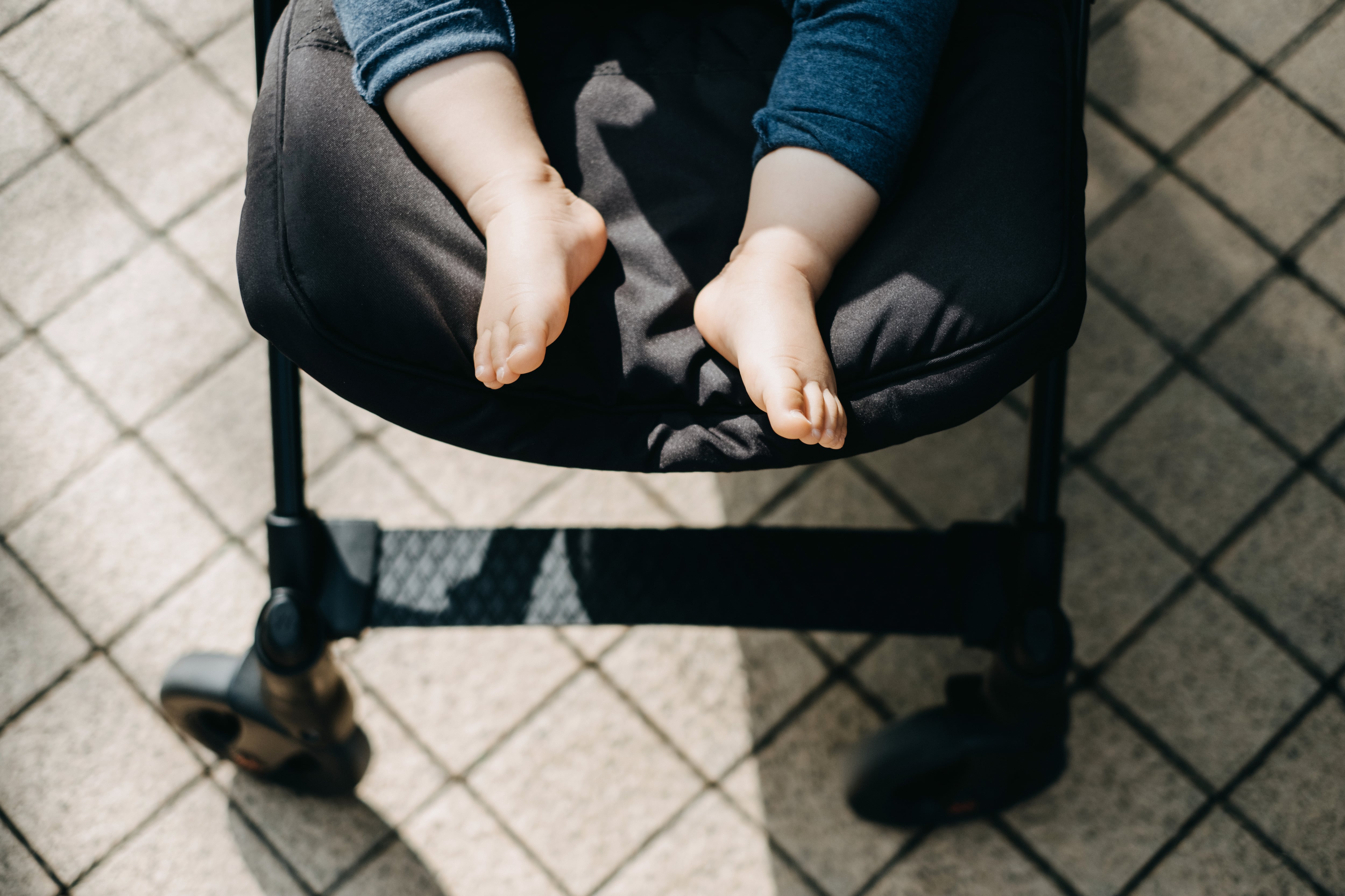 Low section of baby feet resting in baby stroller on street with warmth of sunlight