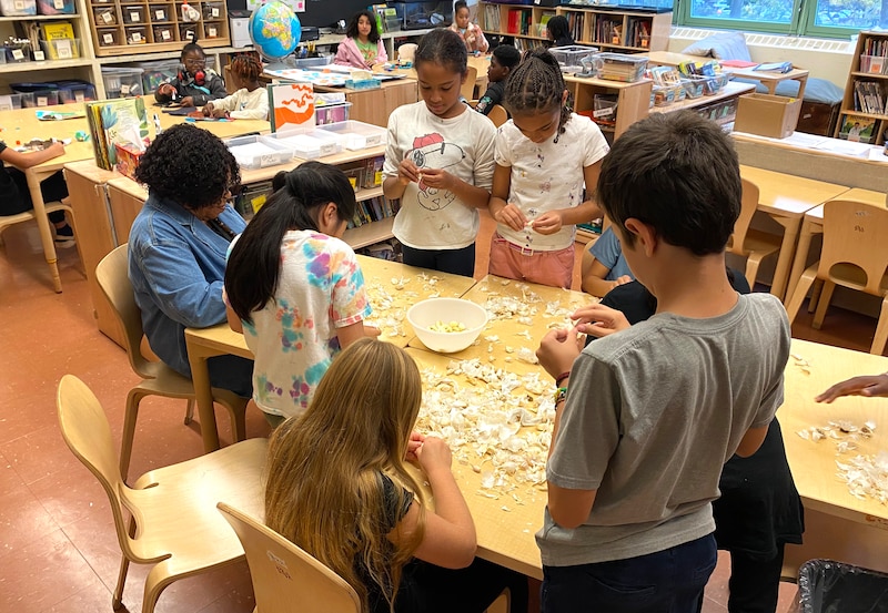 Students and a teacher work at a table in a classroom.