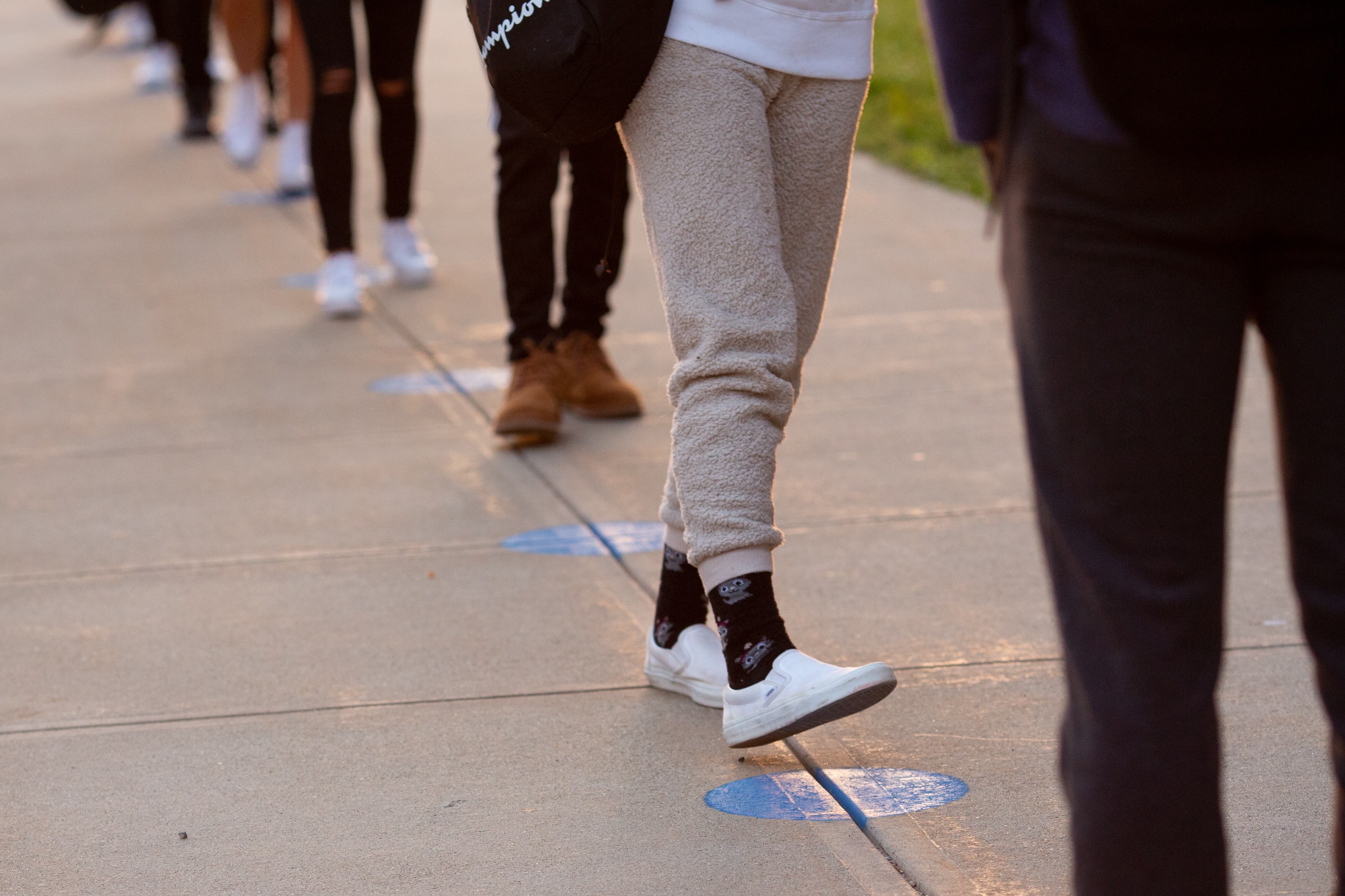 School children in a socially distanced line, only their legs and feet are visible.
