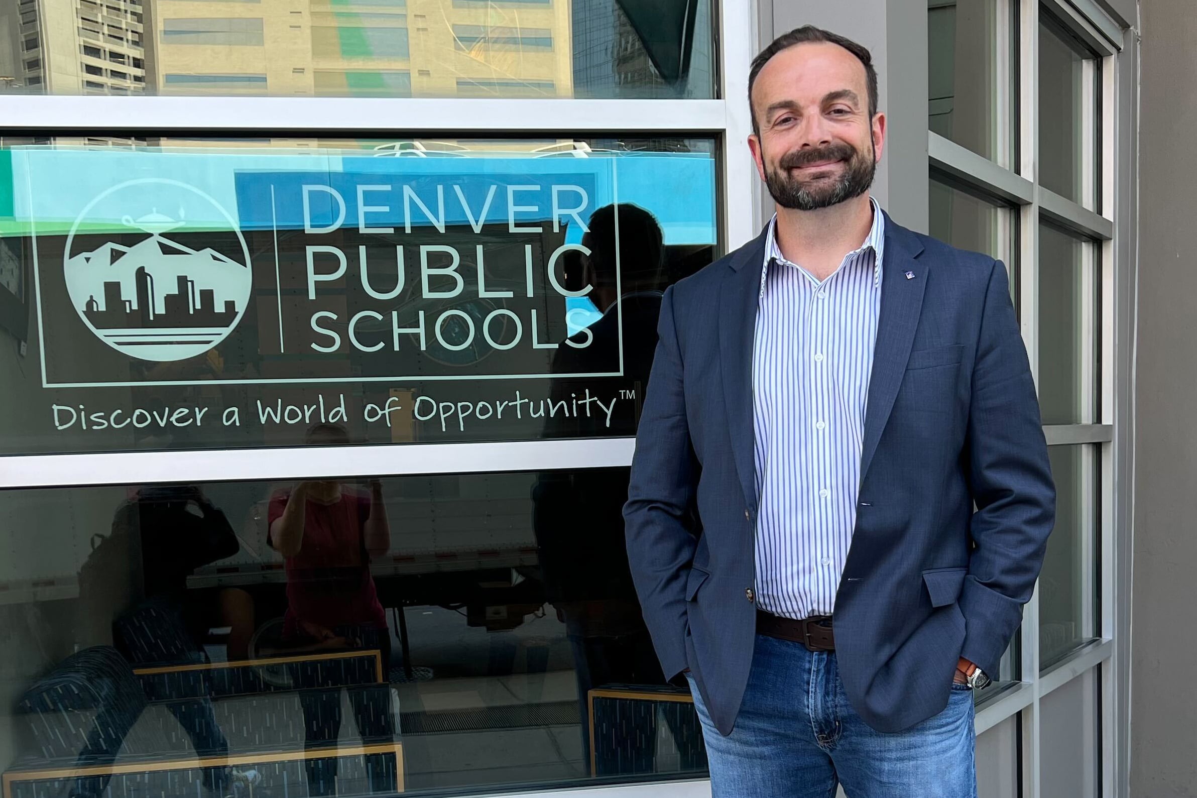 a man in a jacket and jeans stands outside Denver Public Schools headquarters