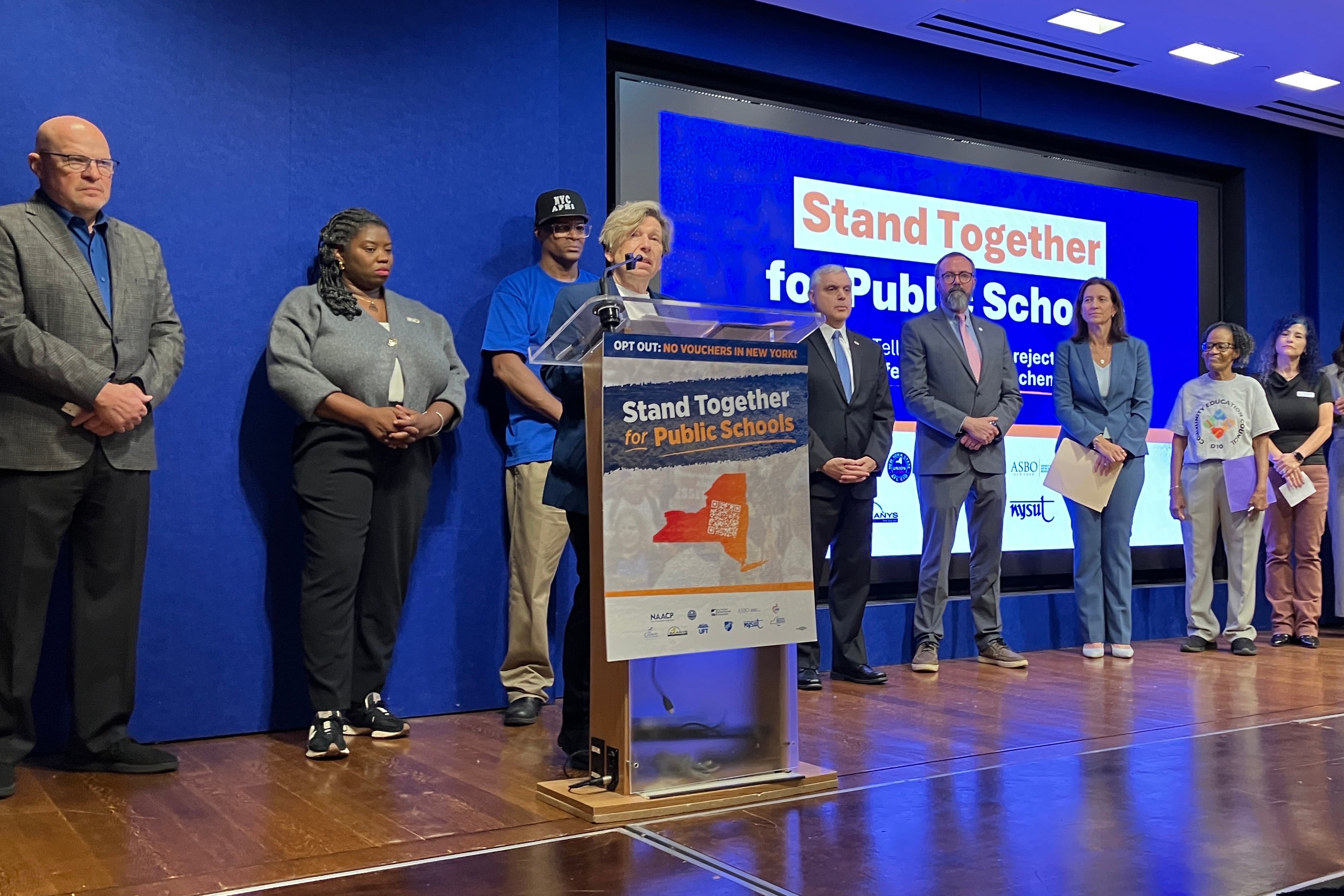 A woman stands at a podium with other people behind her.