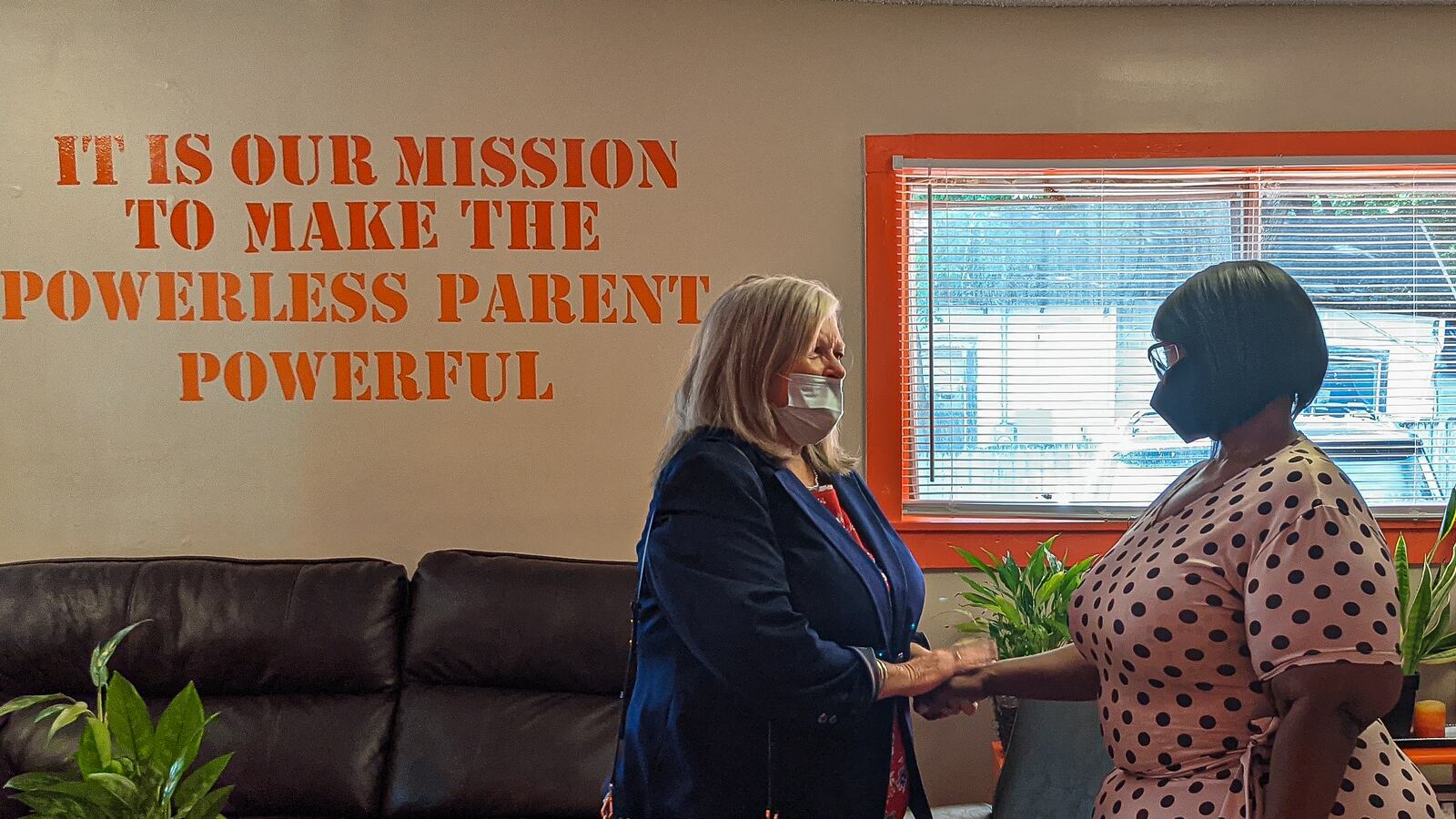 Debra Moody shakes hands with Teresena Medlock at the Memphis Lift headquarters. Painted on the wall behind them is a statement that says, “It is our mission to make the powerless parents powerful.”