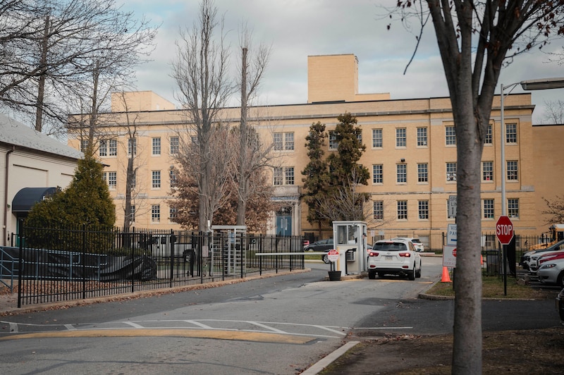 A large tan stone building in the background with a car stopped at a security check point in the foreground.