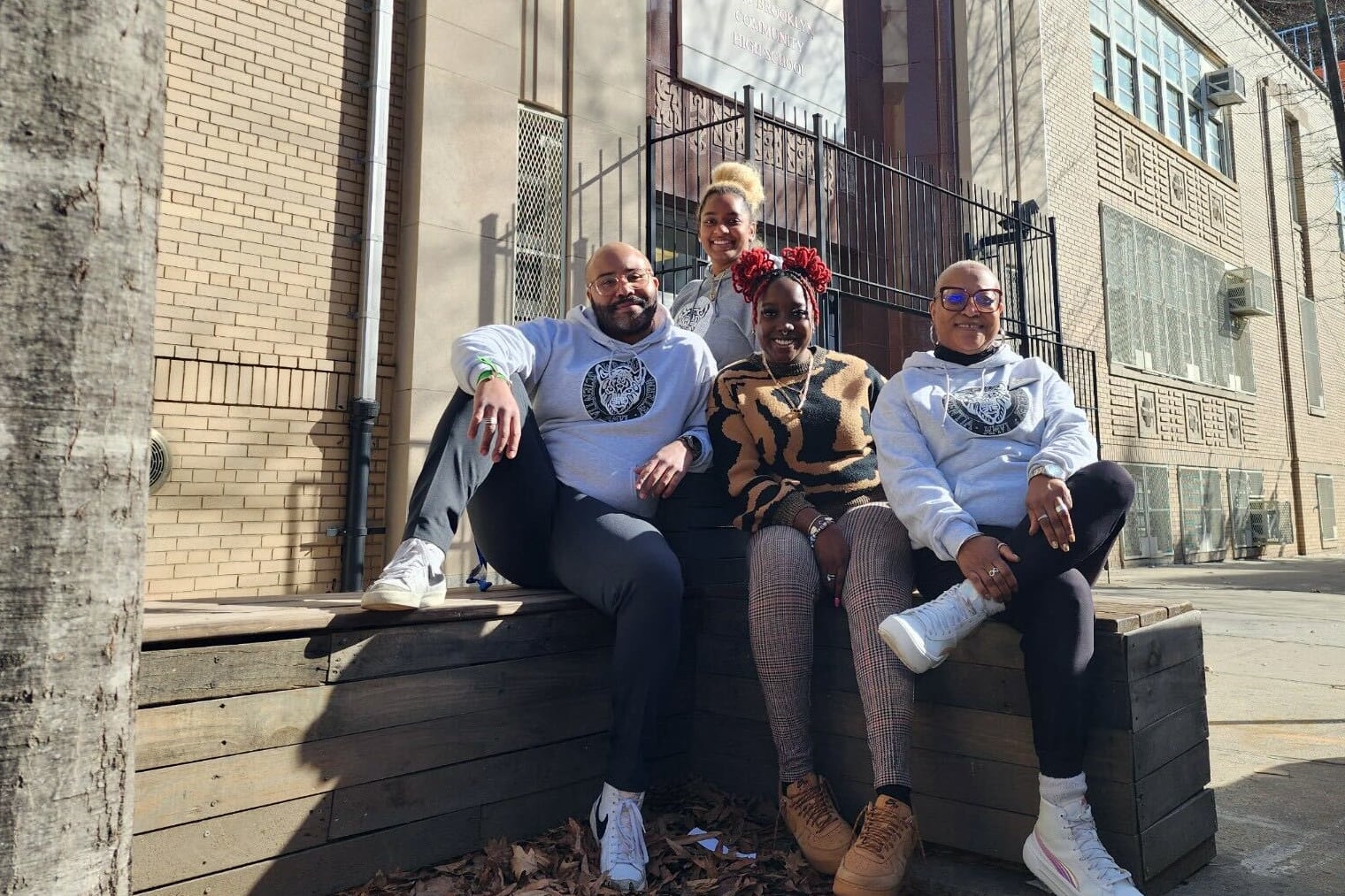 Four adults pose for a photograph outside a large brick building.