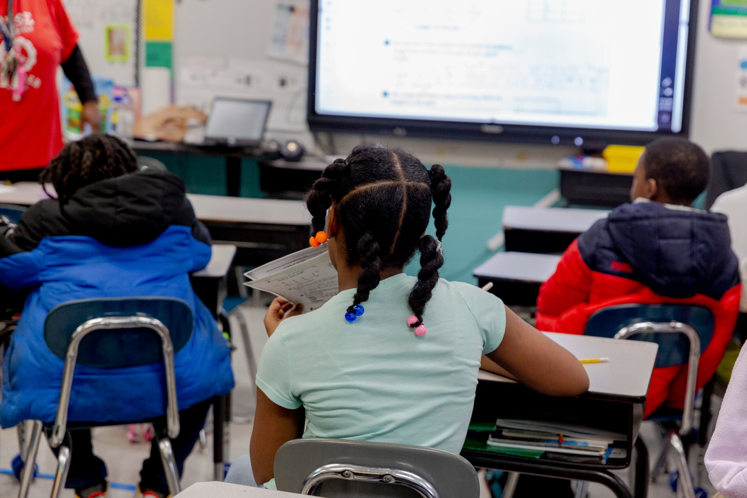 In a view from the back of a classroom, three students sit at their desks.
