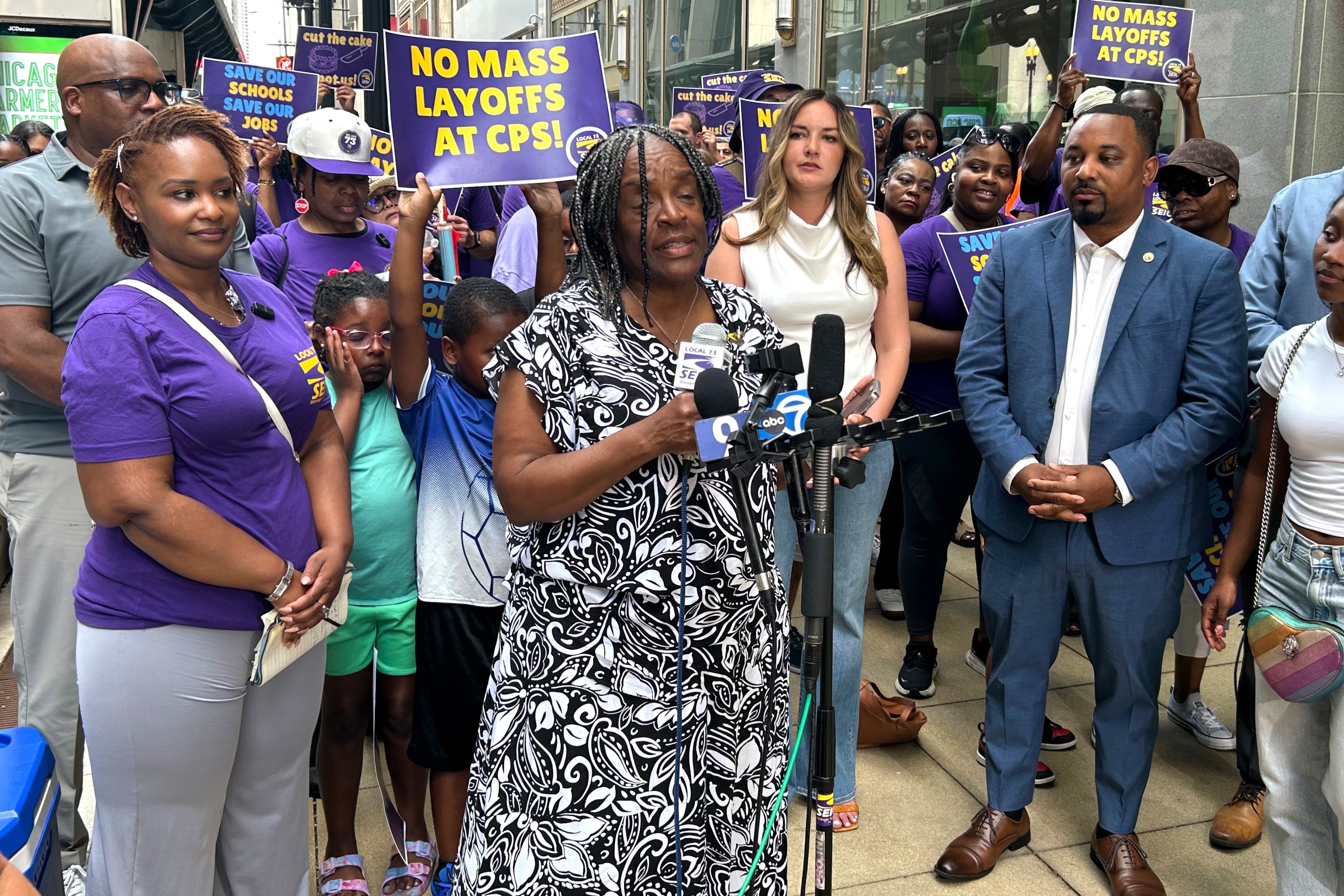 A woman in a black and white dress speaks surrounded by others.