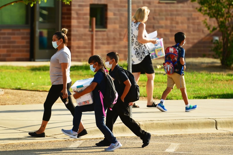 Parents and students wearing masks walk to school.