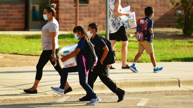 Parents and students wearing masks walk to school.