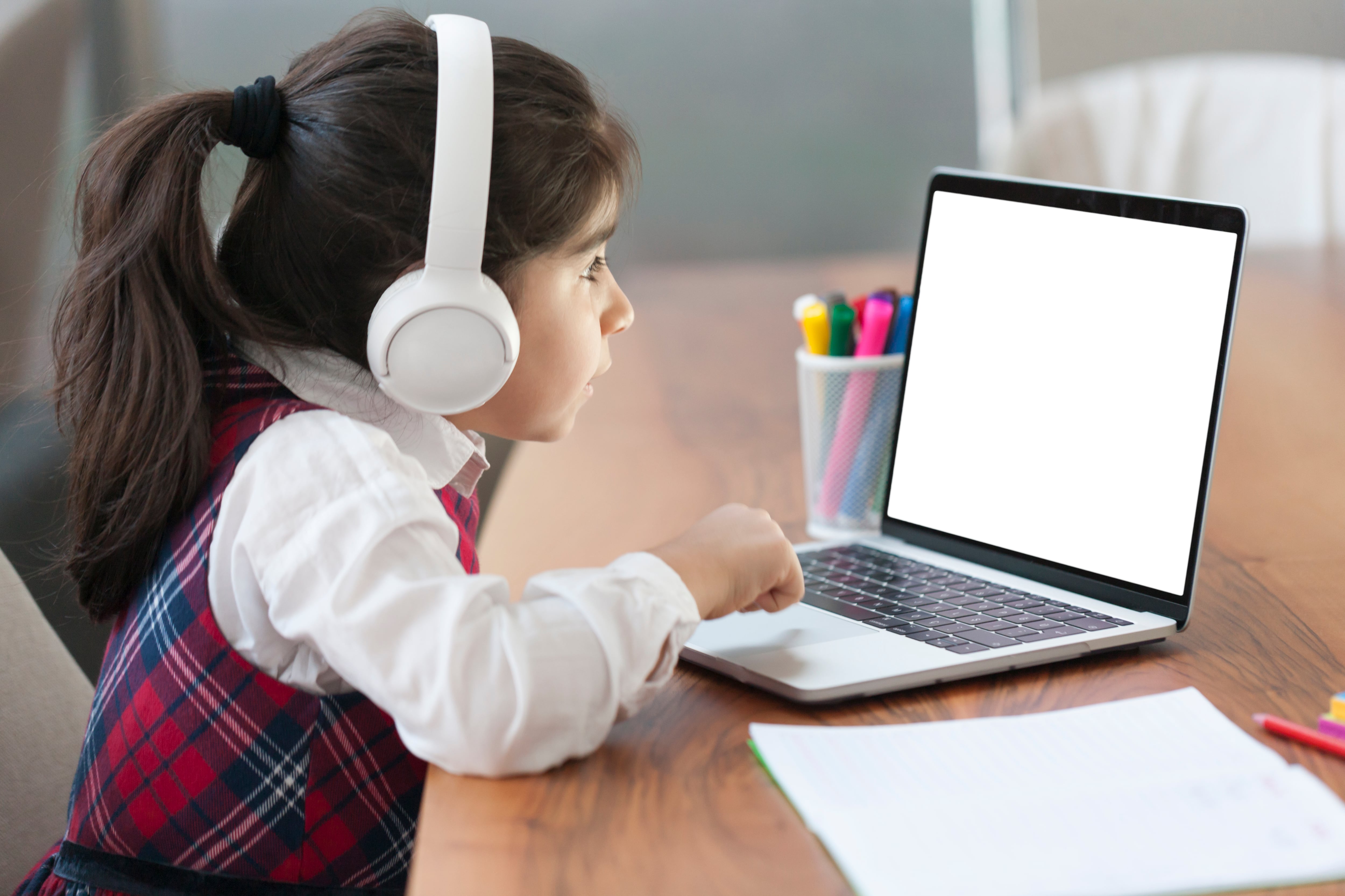 A girl wears headphones in front of a computer.