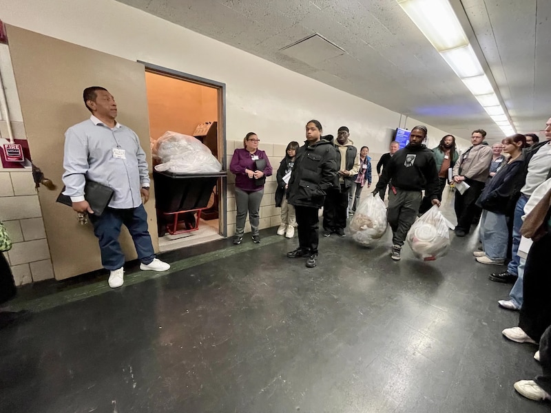 A group of people is gathering in a hallway next to a room with a tilt truck.
