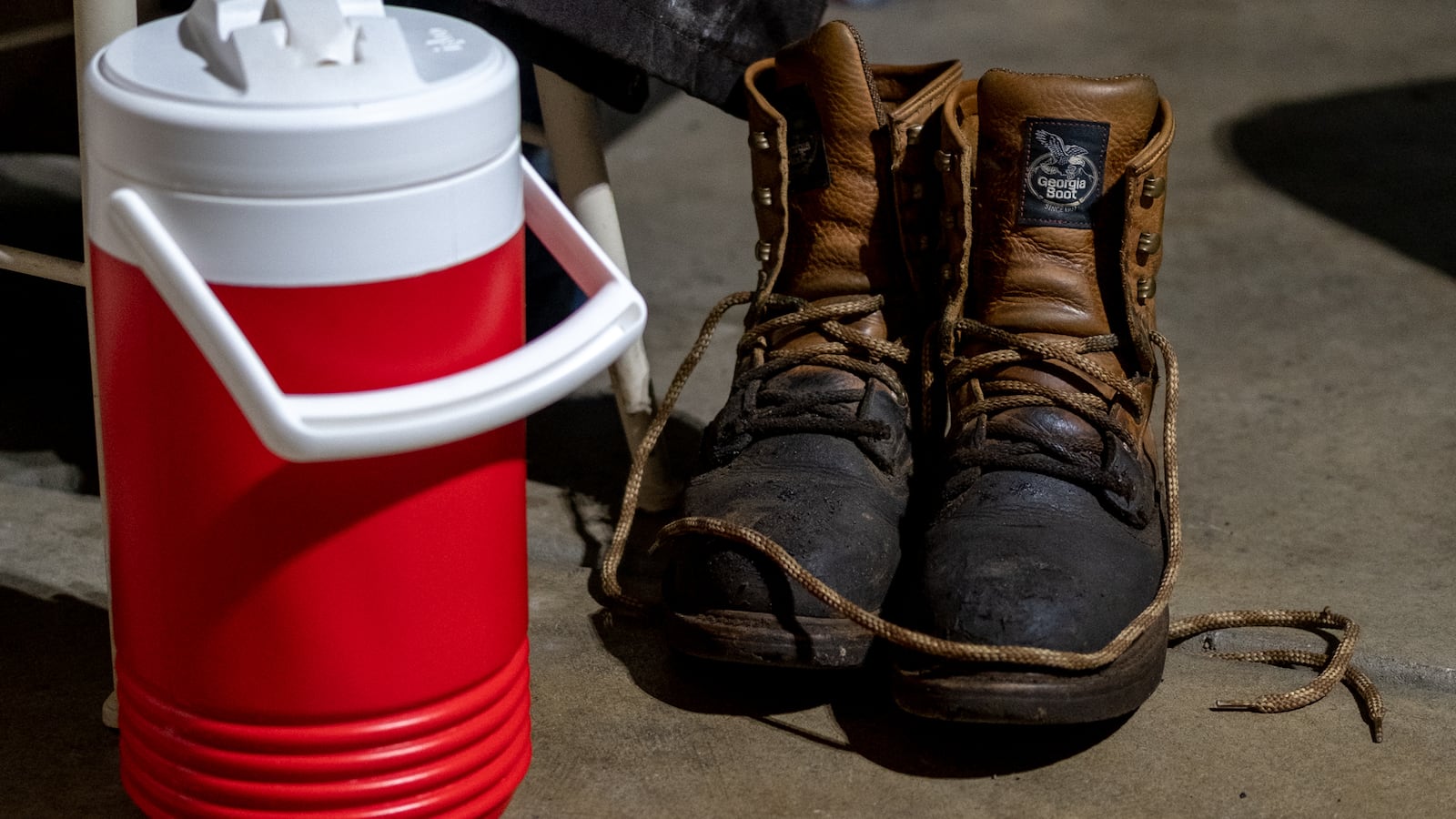 A red and white water jug sits on the floor next to a pair of worn-in work boots.