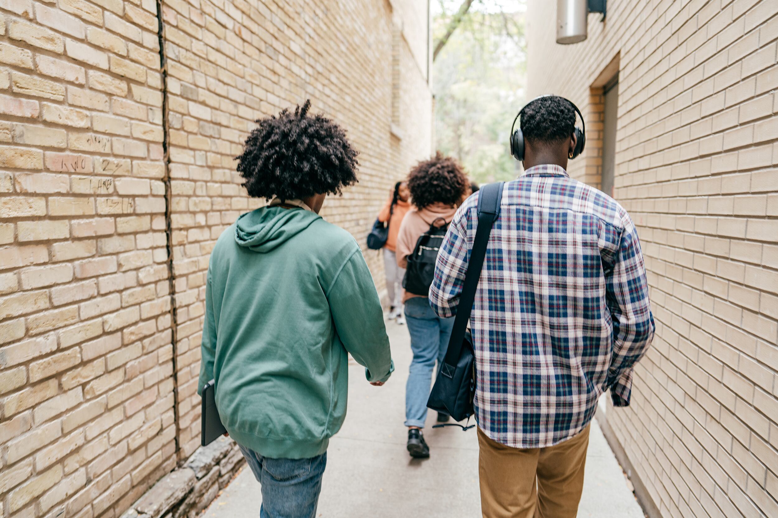 A group of students walk through an outdoor walkway with tan brick walls on each side.