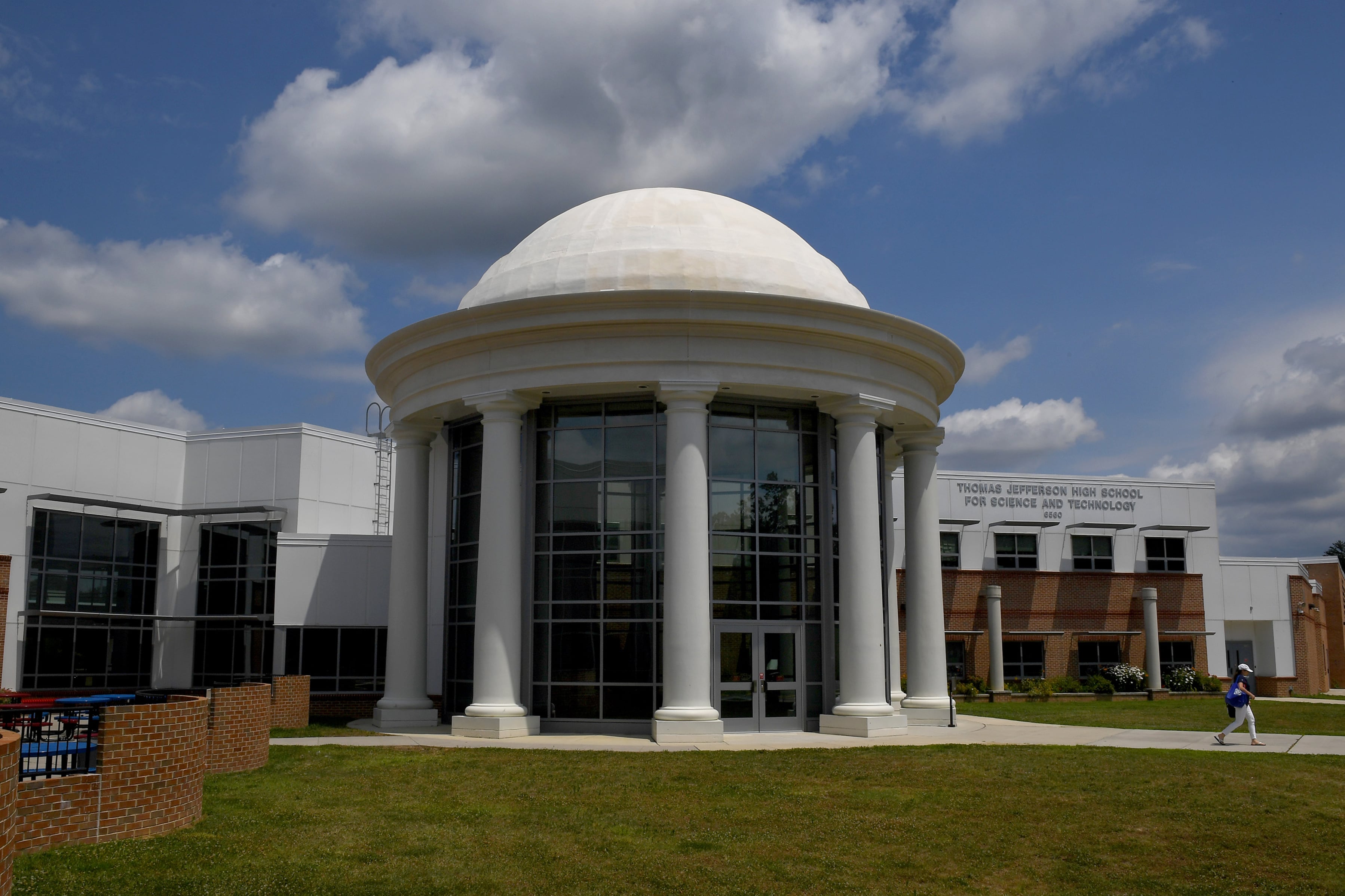 A large white stone school building on a sunny day with some large fluffy clouds overhead.