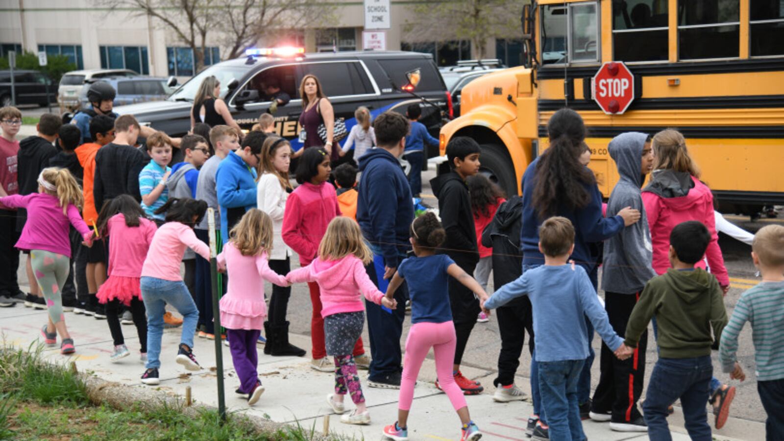 Students are escorted to a school bus in front of STEM School Highlands Ranch after a shooting.