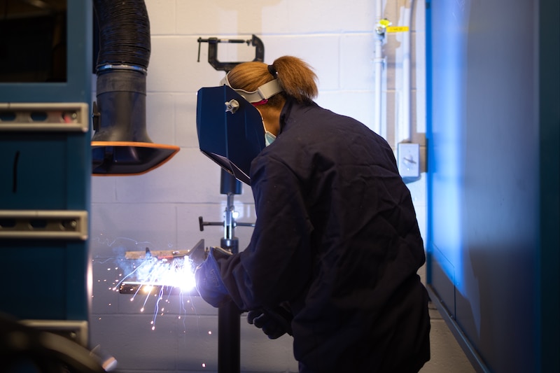 A person bends over while welding.