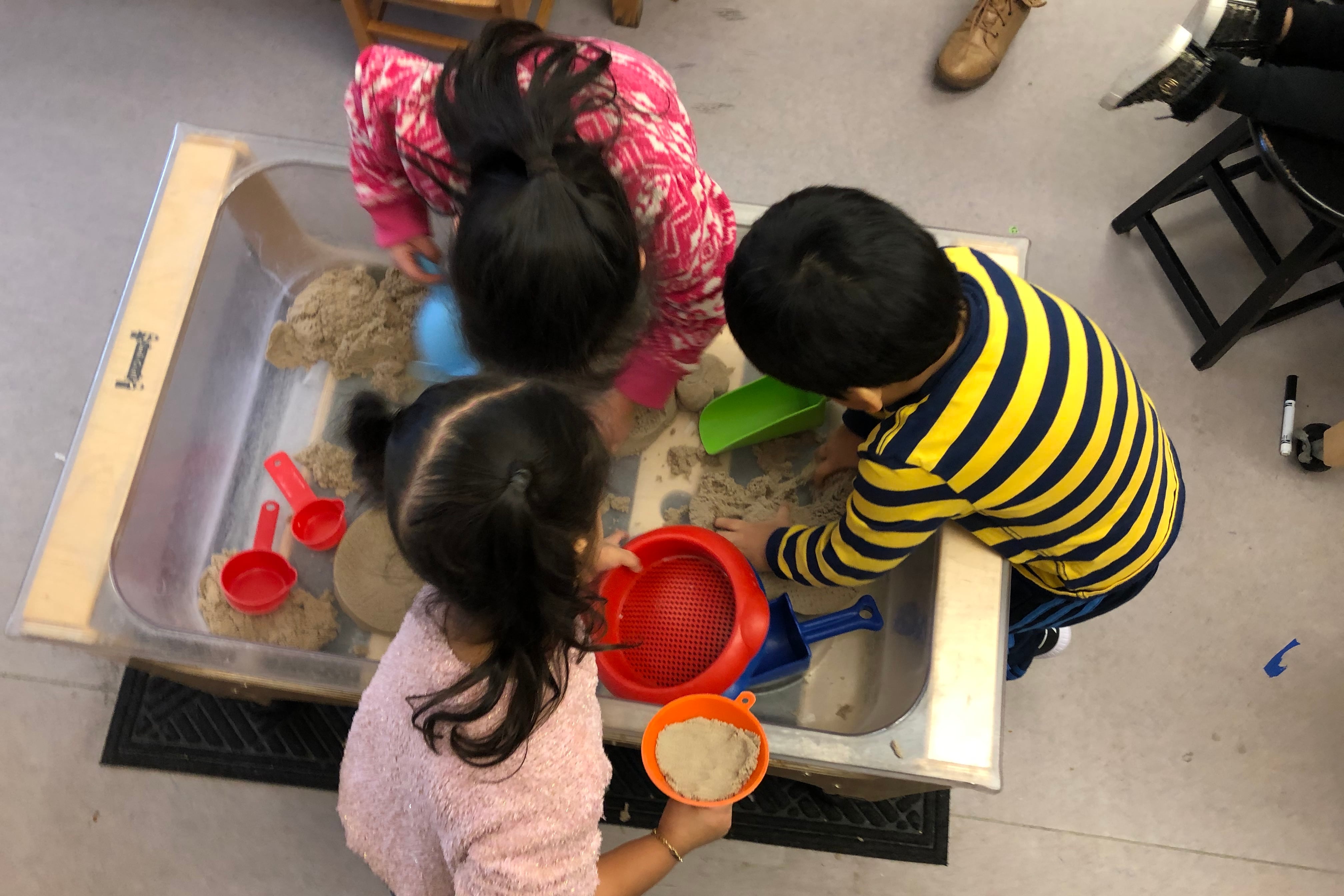 A bird's eye view of three young students playing in a sand table.