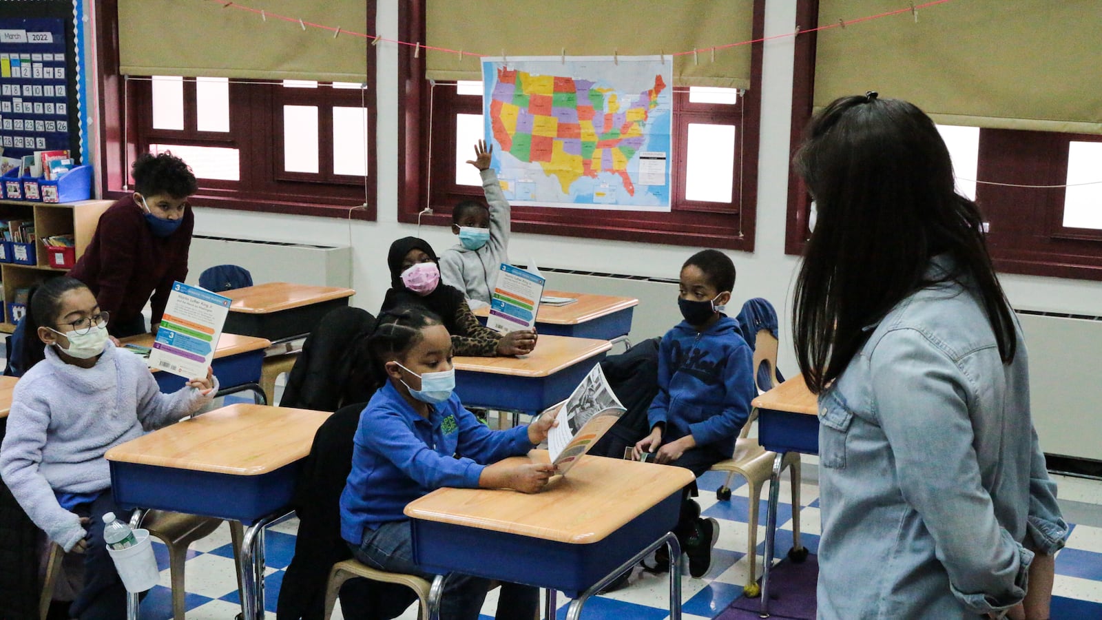 A teacher leads her class of young students as they read books at their desks.
