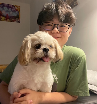 A high school student wearing glasses and a green shirt poses while holding a small, white dog.