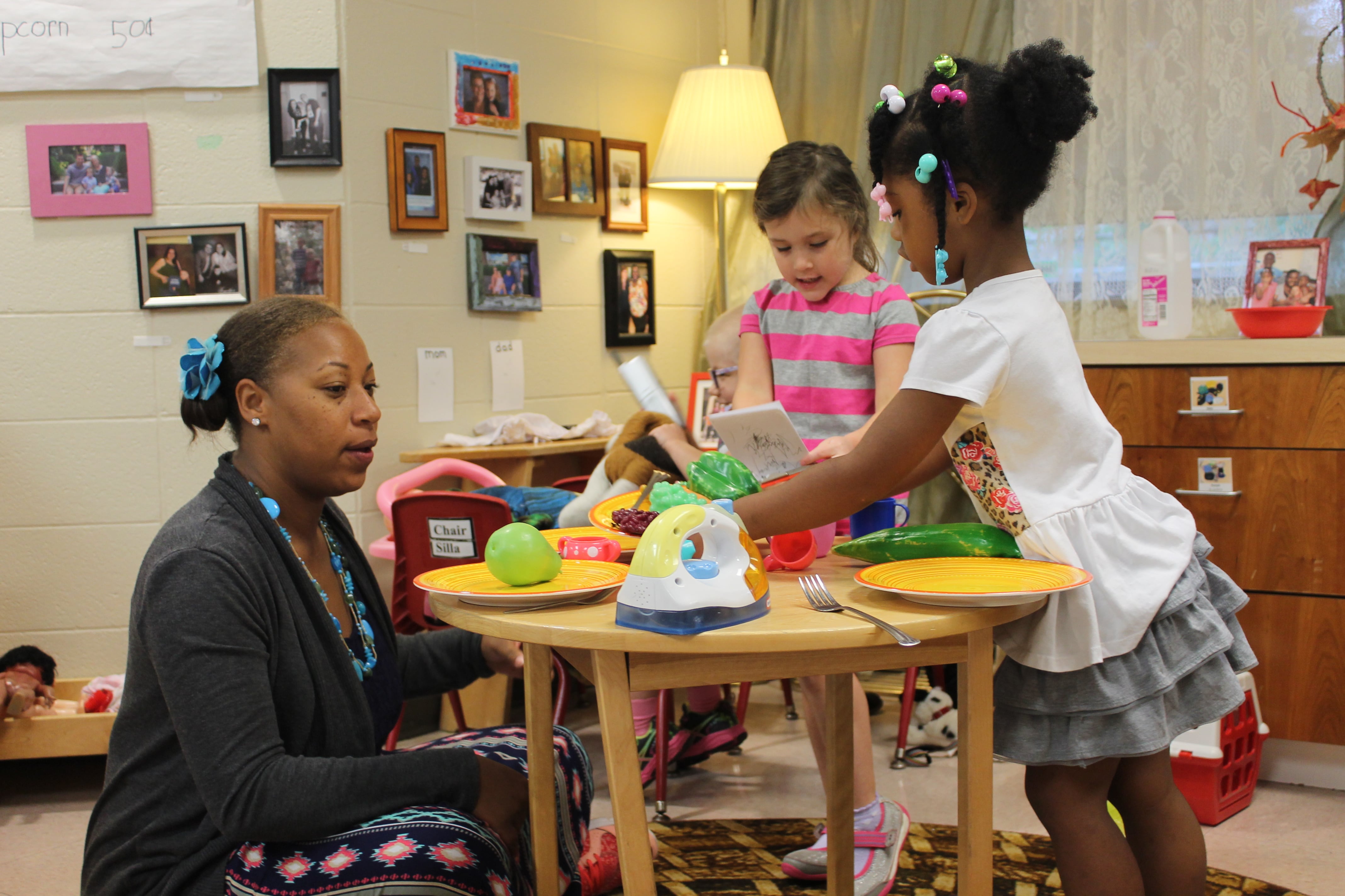 A teacher sits with two preschoolers while they play in a preschool classroom at the Day Early Learning Lilly Center.