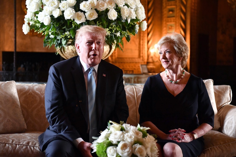 Two adults in business clothes sit on a couch inside a room filled with white roses.