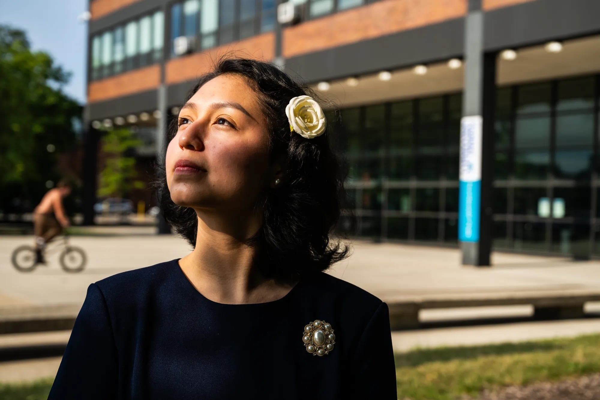 A young woman with a flower in her hair looks to her right.