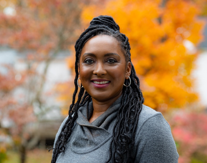 A portrait of a woman in a gray shirt in front of fall leaves.