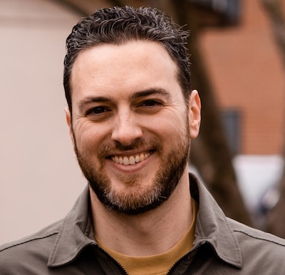 Headshot of man with dark hair and beard wearing a khaki shirt.