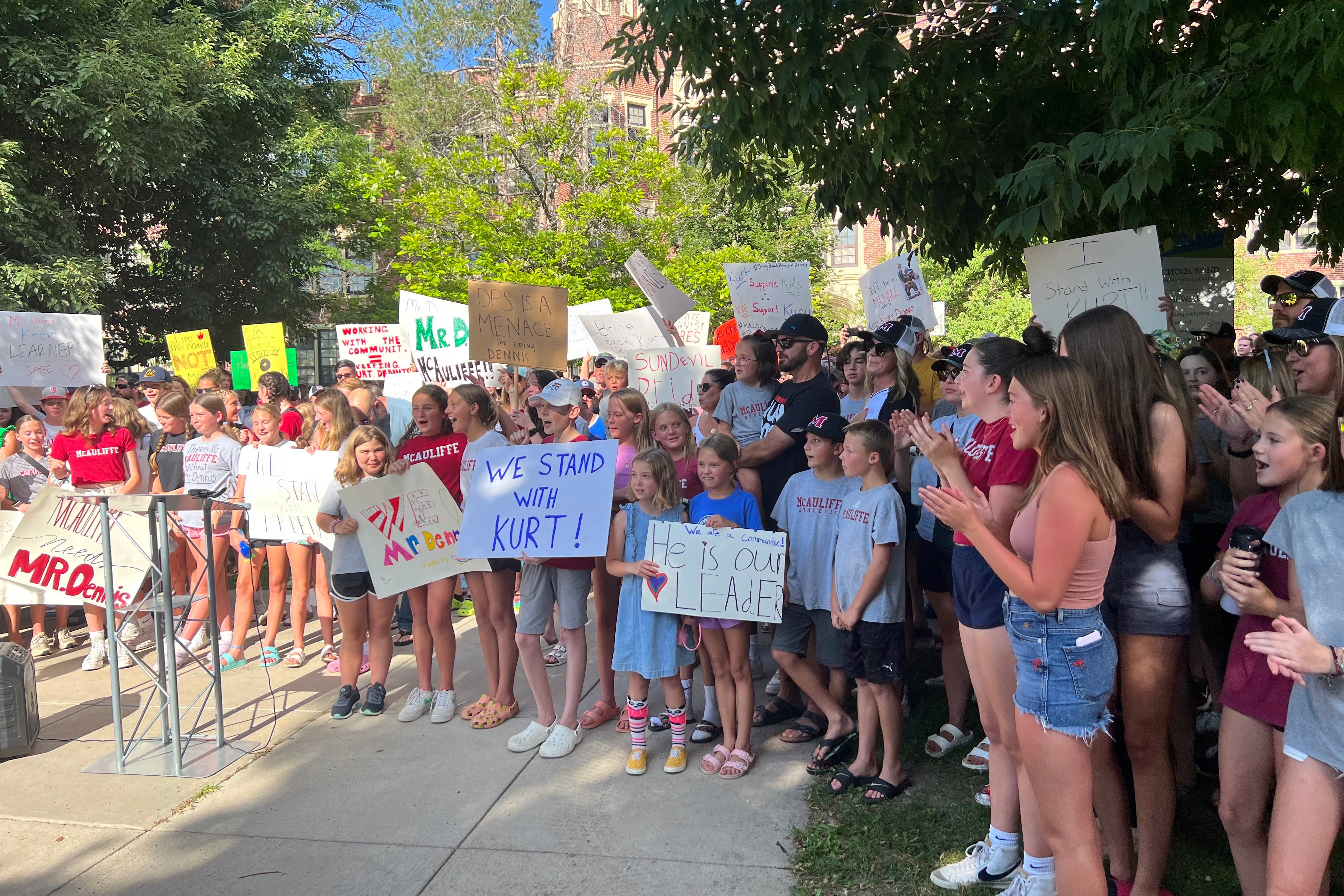 A group of people stand outside a middle school holding homemade signs.