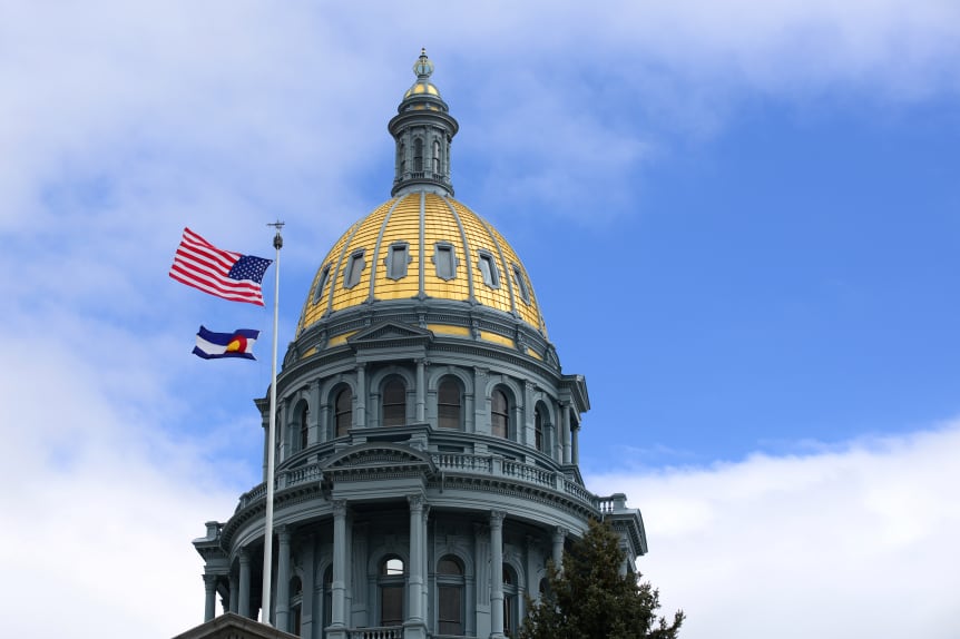 Colorado state Capitol building in Denver, Colorado, with the U.S. and state flags in front of a cloudy sky