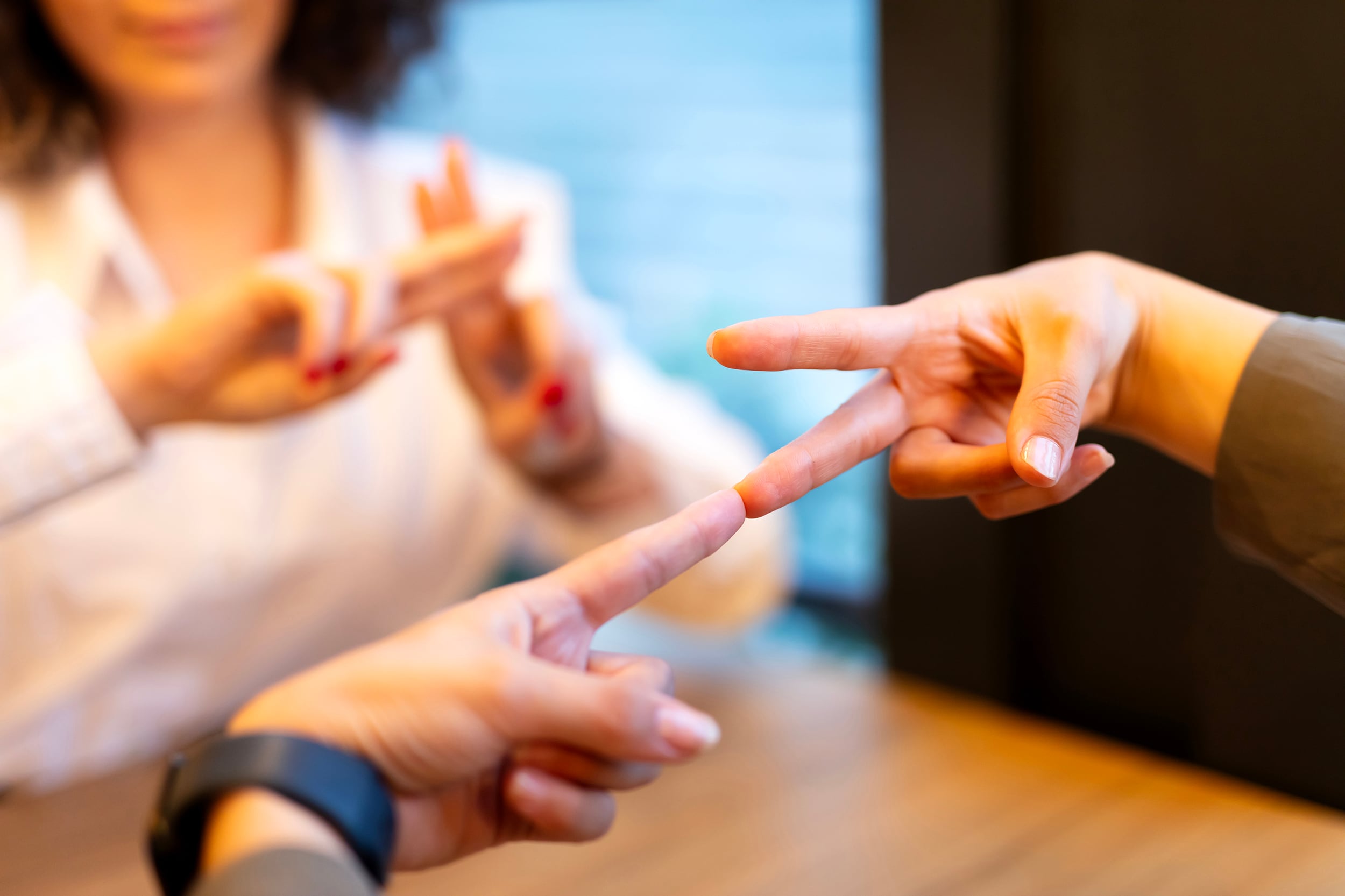 An up close photograph of a pair of hands signing to a person in the background.