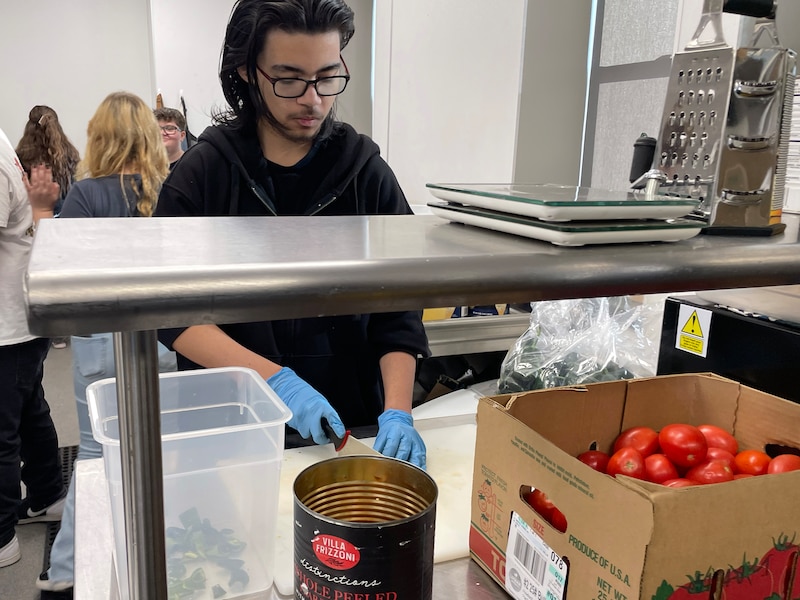 A high school students chops tomatoes.