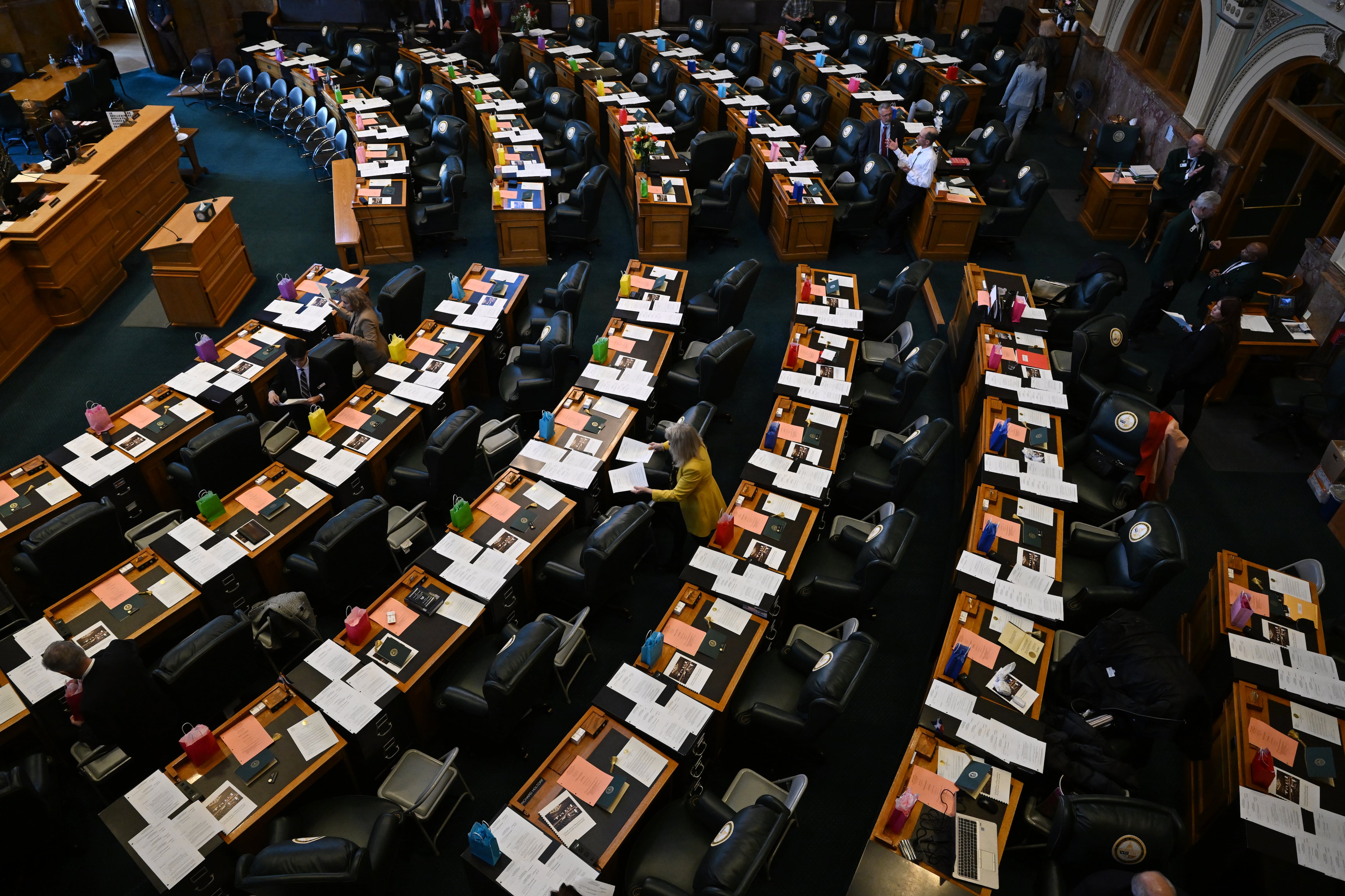 About a dozen people walk between the rows of desks in the Colorado House chambers in Denver, Colorado.