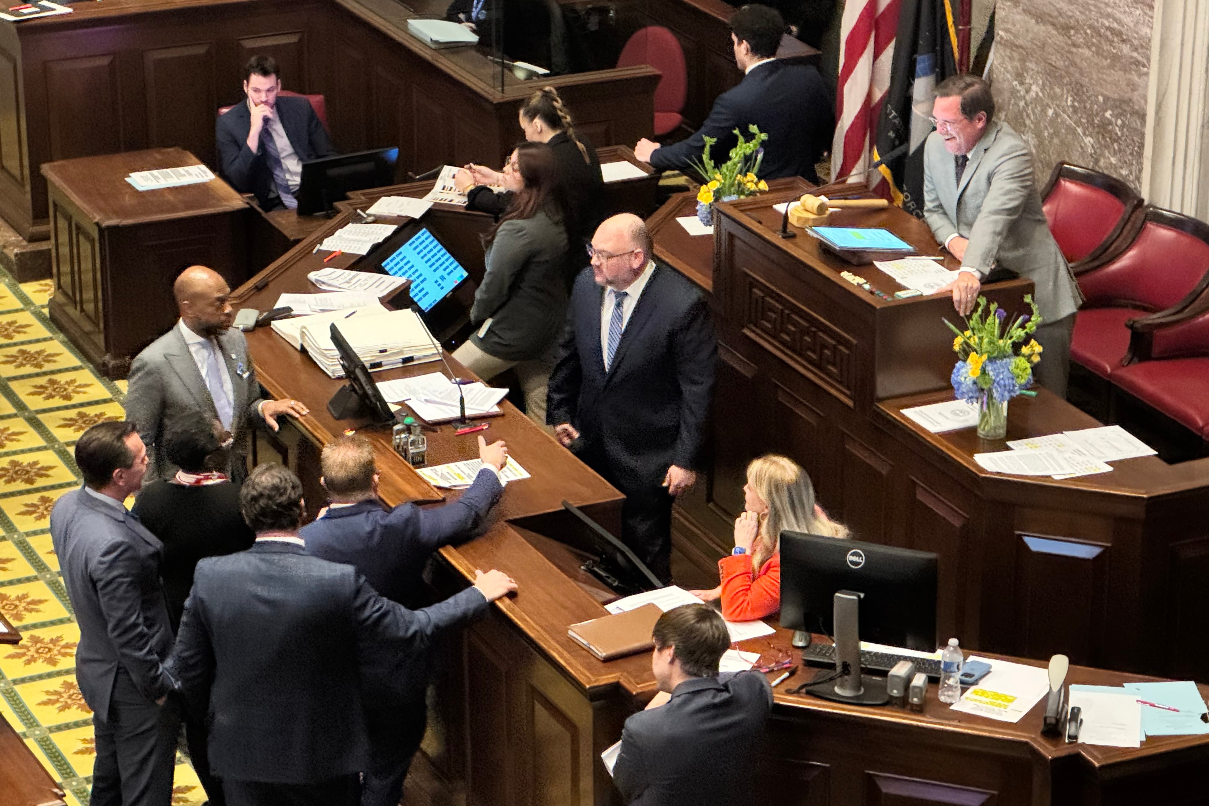 A group of people in suits stand on the floor of a capitol building.