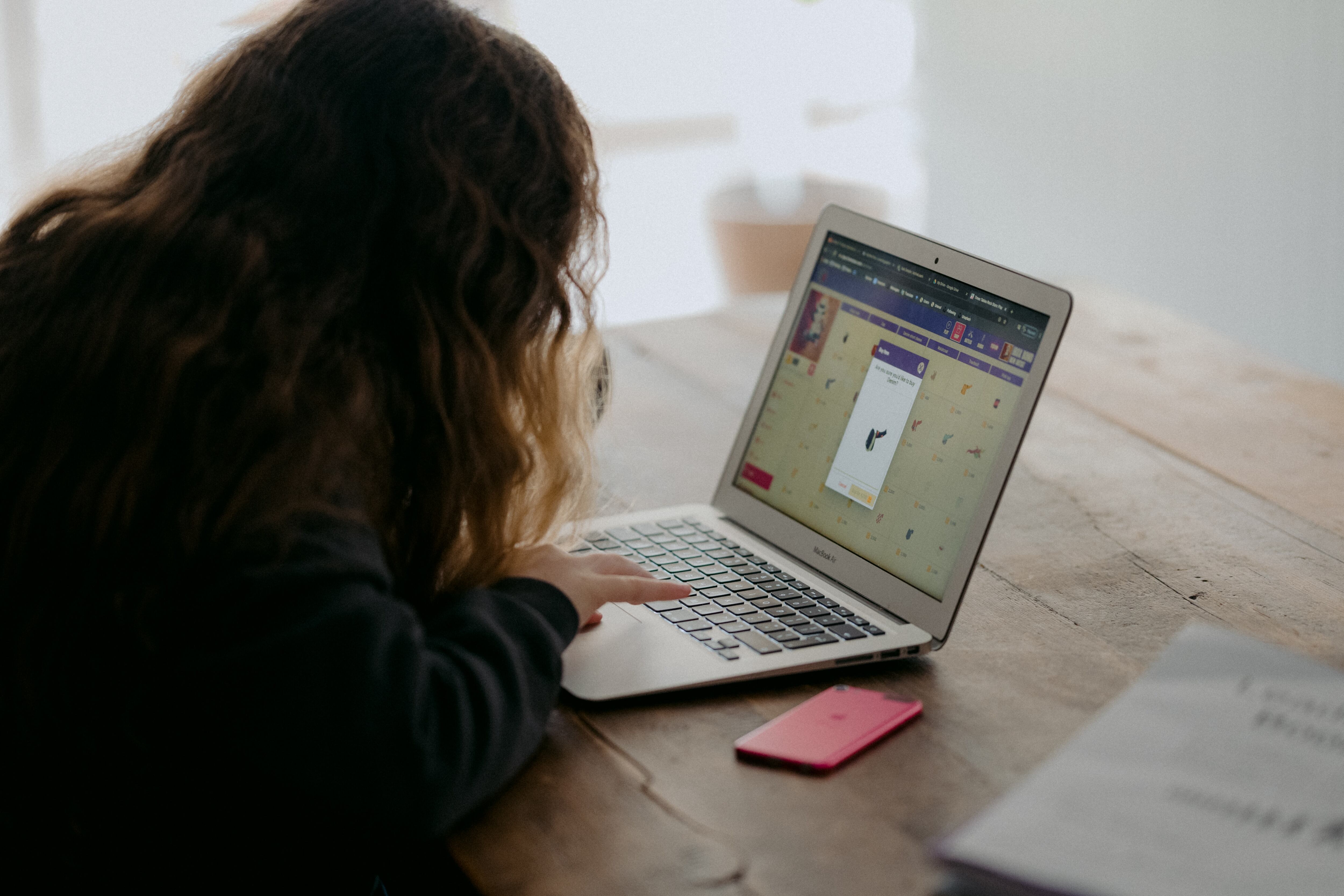 Young girl sitting at table doing homework on a laptop.