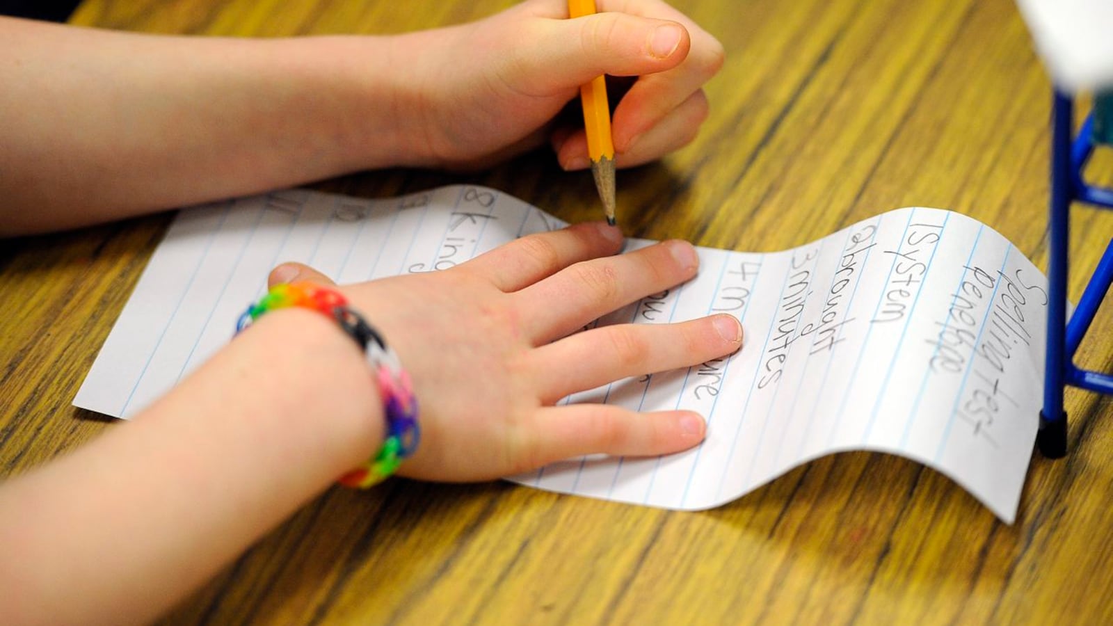 A close-up of a young student's hands as they work on a spelling test.