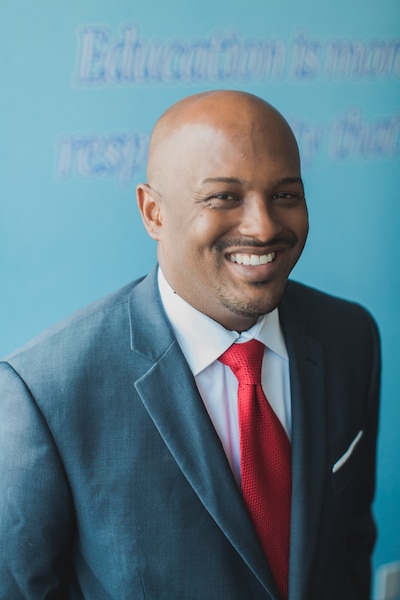Headshot of a man wearing a gray suit, a white shirt and a red tie.