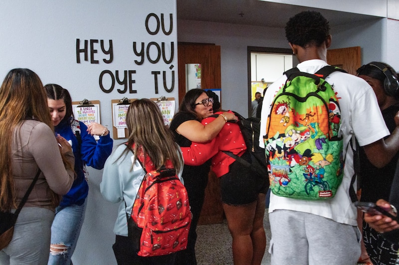 Two women hug surrounded by students in a hallway.
