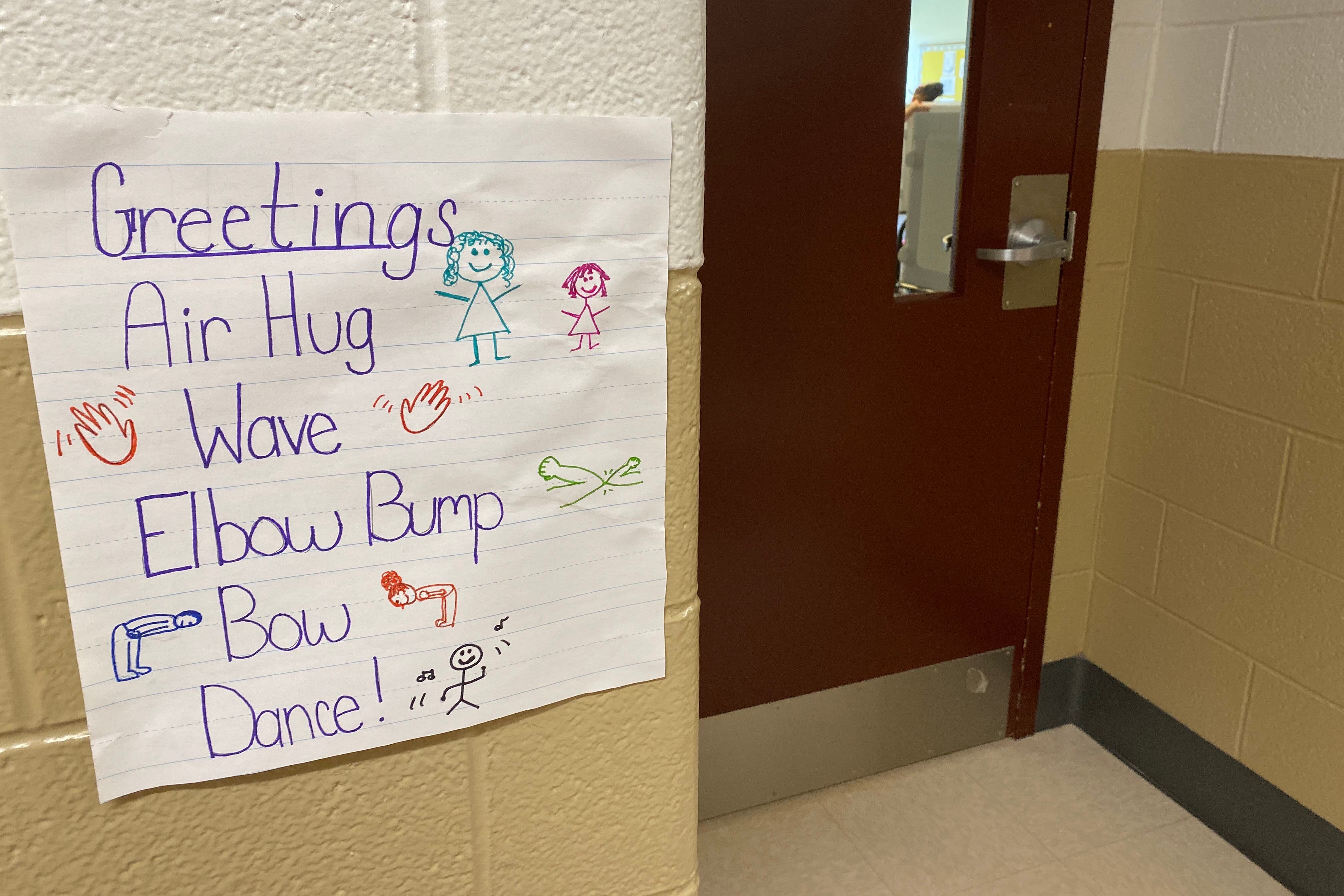 A sign in a hallway by a door at Tindley Summit Academy in Indianapolis says “Air hug, wave, elbow bump, bow, dance”