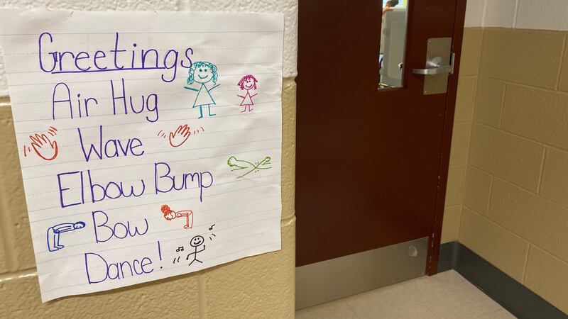 A sign in a hallway by a door at Tindley Summit Academy in Indianapolis says “Air hug, wave, elbow bump, bow, dance” 
